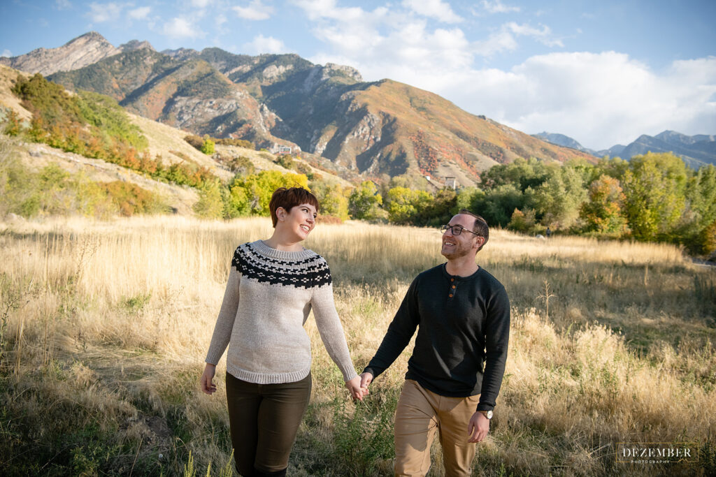 Couple walks hand in hand in field with mountains