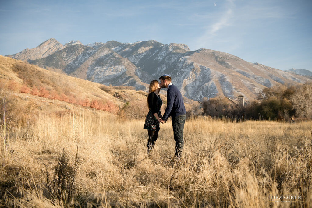 Couple kisses in golden field with mountains in background