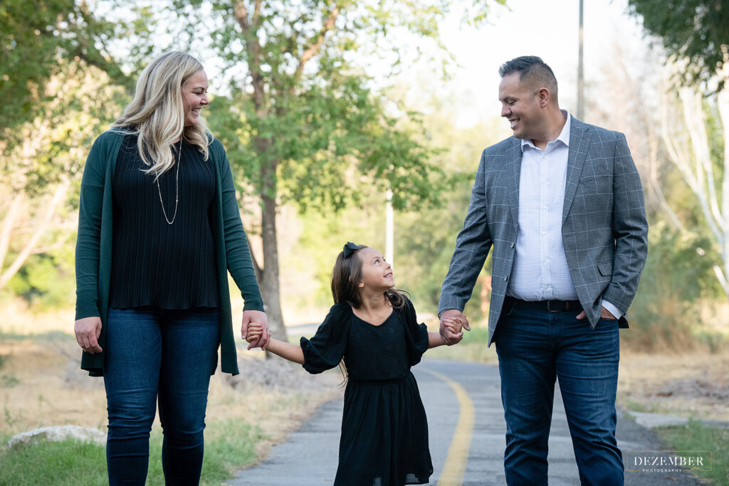 Girl walks hand in hand with her parents on the Jordan River Parkway