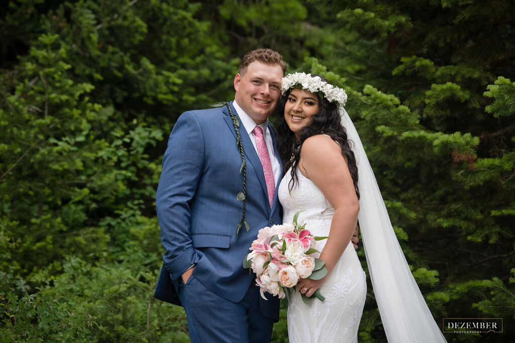 Couple poses in green trees with Polynesian bridal wear