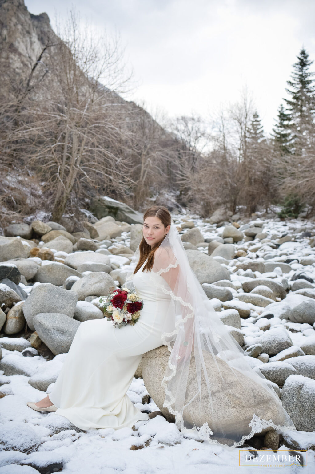 Snowy intimate wedding bride sits on rock