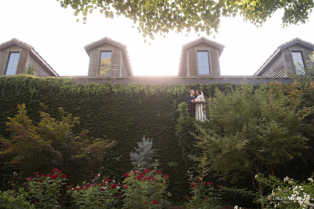 Bride and groom stands on balcony at Ivy House with big living wall and rose bushes